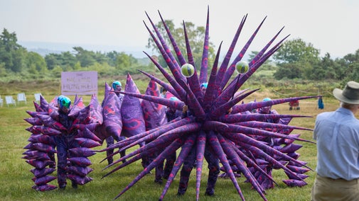 Giant puppet with spiky purple and pink body and giant green eyes.